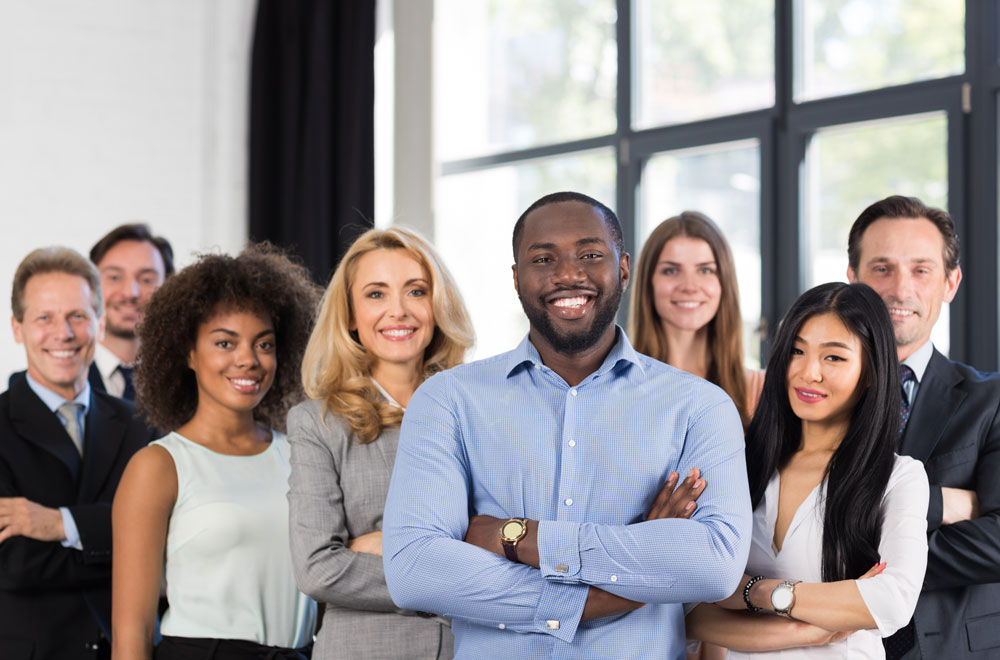 an image of a diverse group of coworkers in business casual attire standing together in front of a large floor to ceiling window in the background