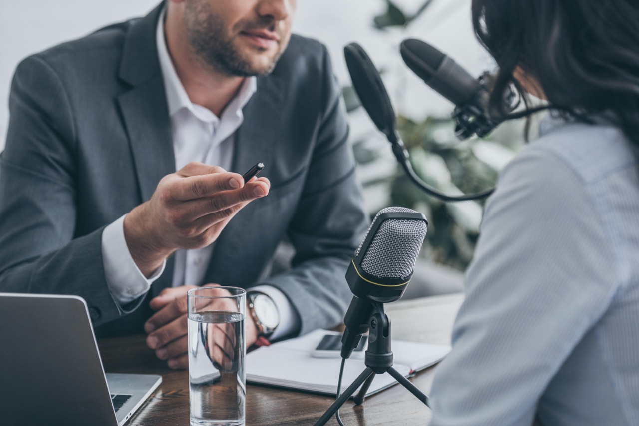 cropped view of radio host gesturing while interviewing businesswoman in broadcasting studio