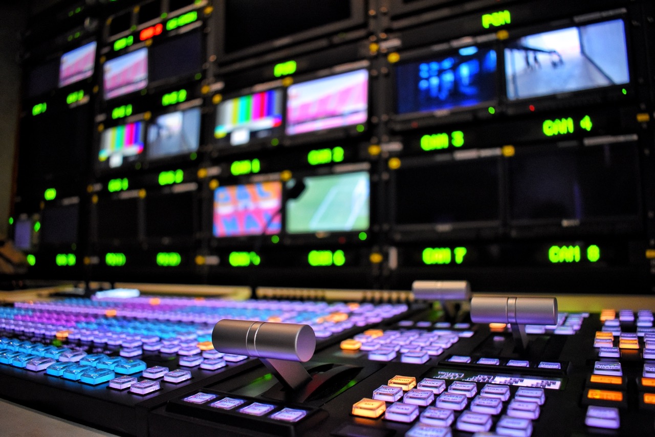 a dimly lit producers mixing table with lots of colorful knobs and buttons